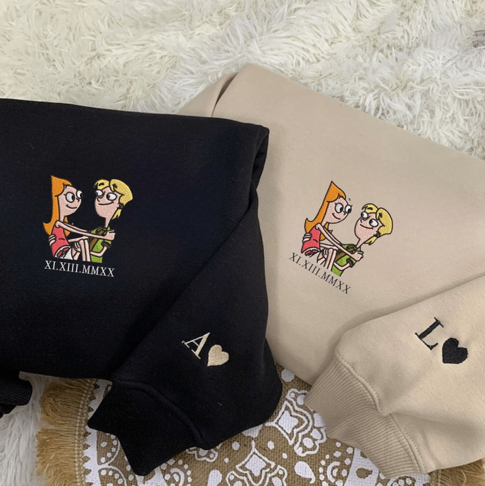 Couple hoodies in beige and black with heart embroidery and cartoon illustration.