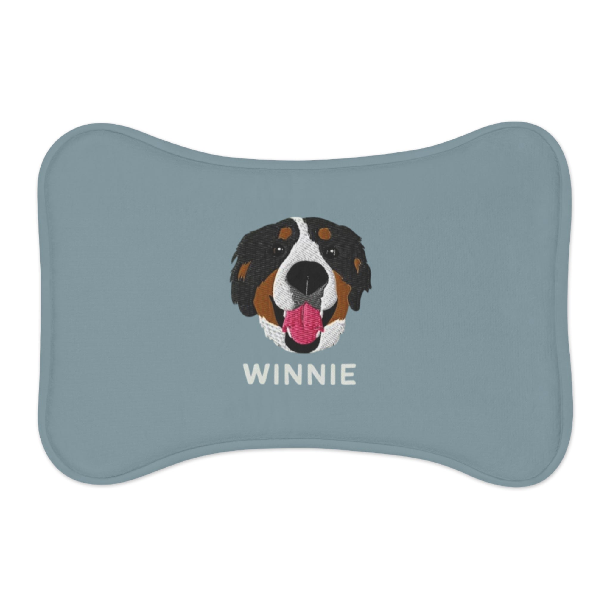 Blue bone-shaped custom feeding mat featuring an embroidered-style portrait of a Bernese Mountain Dog with the name “Winnie” printed underneath.

