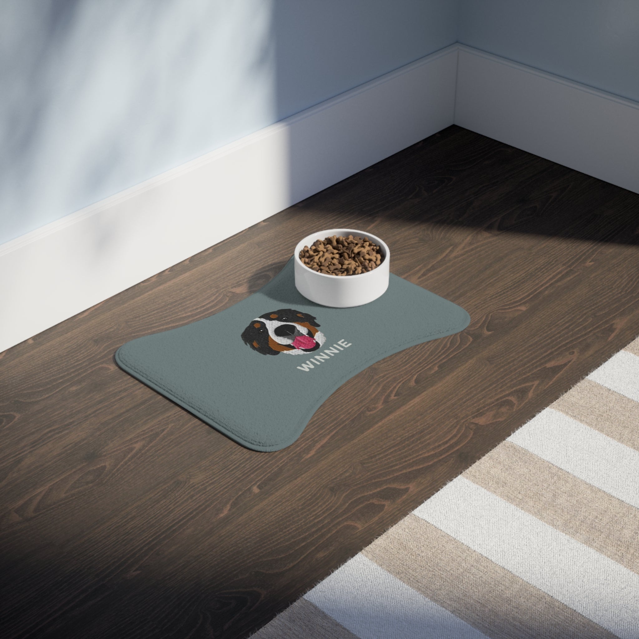 Blue bone-shaped custom feeding mat featuring an embroidered-style portrait of a Bernese Mountain Dog with the name “Winnie” printed underneath.

